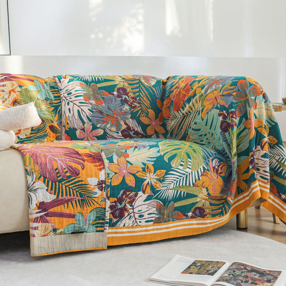A brightly colored tropical-themed throw blanket with a bold floral and leaf pattern draped over a white sofa, styled for a cozy, decorative look.