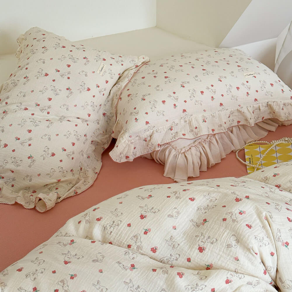 A partial view of a bed showing two pillows and a duvet cover from cotton muslin set, highlighting the soft fabric, delicate ruffles, and cute bunny print.