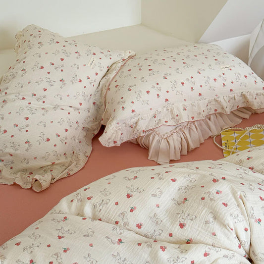 A partial view of a bed showing two pillows and a duvet cover from cotton muslin set, highlighting the soft fabric, delicate ruffles, and cute bunny print.