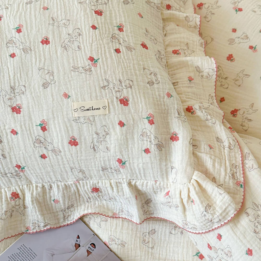 A detailed close-up of a pillow from the twin-size cotton muslin bedding set, featuring the charming bunny and red floral pattern, ruffled edge