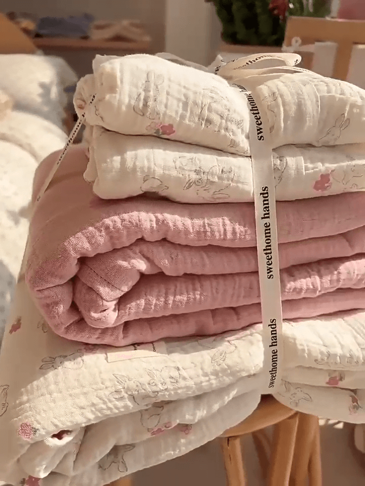 A neatly folded stack of cotton muslin duvet cover set, tied with a ribbon, showing the bunny and floral print and the ruffled edges.