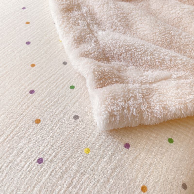 A close-up texture shot of a warm winter baby blanket, showing the soft fleece on one side and the multicolored polka dot pattern on the other.