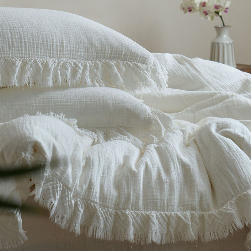 A close-up shot of the white cotton gauze bedding set, focusing on the soft, crinkled texture and the layered fringe on the duvet cover and pillows.