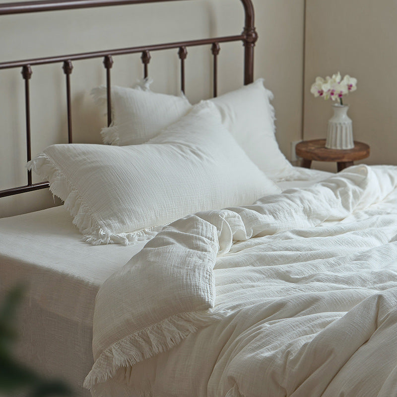 A lifestyle photo of the complete white cotton gauze bedding set on a bed with a dark metal headboard, showcasing the full ensemble in a natural light setting.