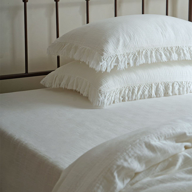 A detailed image of two stacked pillows from the white cotton gauze bedding set, highlighting the delicate fringe border and the fine muslin texture.