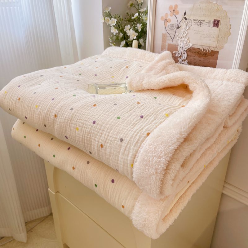 A warm winter baby blanket with colorful polka dots and a soft fleece lining, folded on a cabinet.