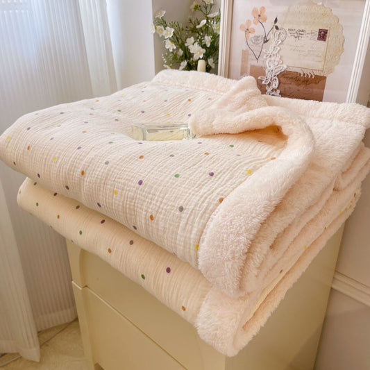 A warm winter baby blanket with colorful polka dots and a soft fleece lining, folded on a cabinet.