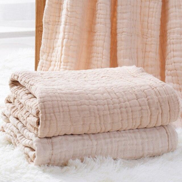 A folded 6-layer thick organic colored cotton muslin baby blanket on a white fluffy rug, showcasing the natural beige color and cozy texture