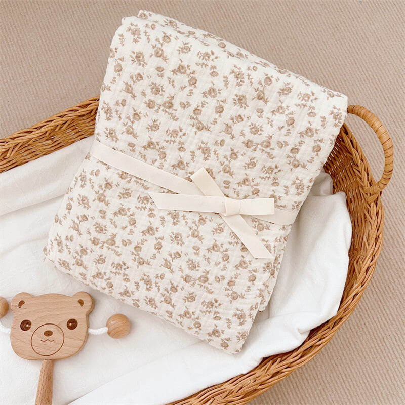 Folded camellia floral cotton muslin baby blanket tied with a ribbon.