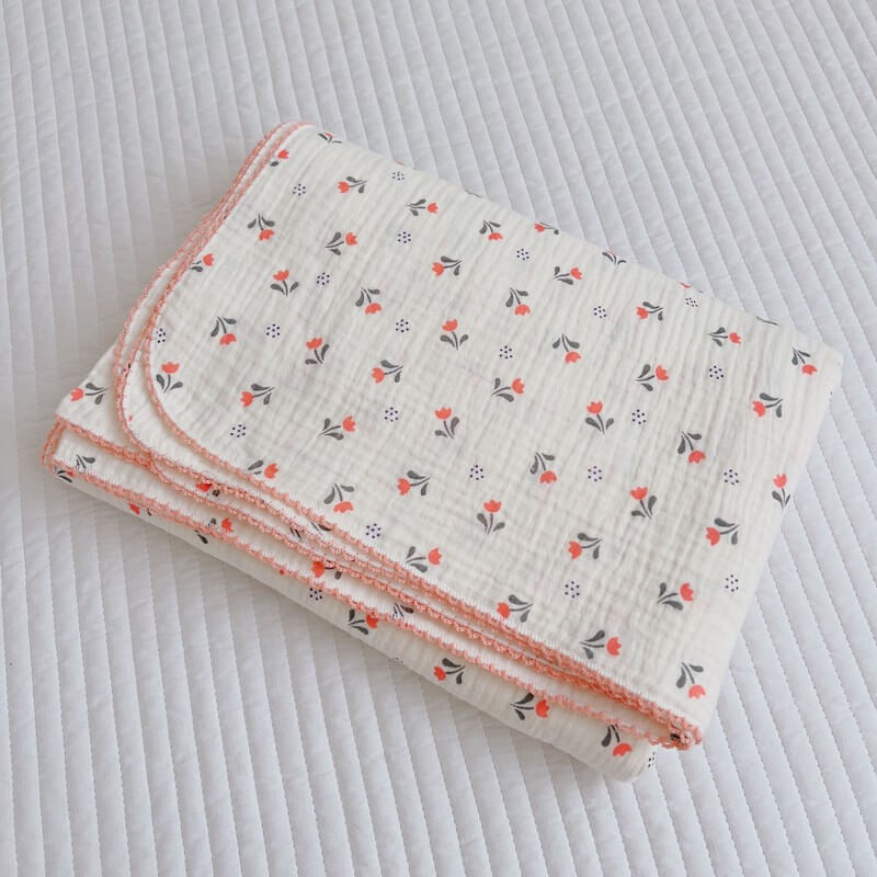 A neatly folded muslin receiving blanket featuring a vibrant tulip floral pattern with red and grey motifs.
