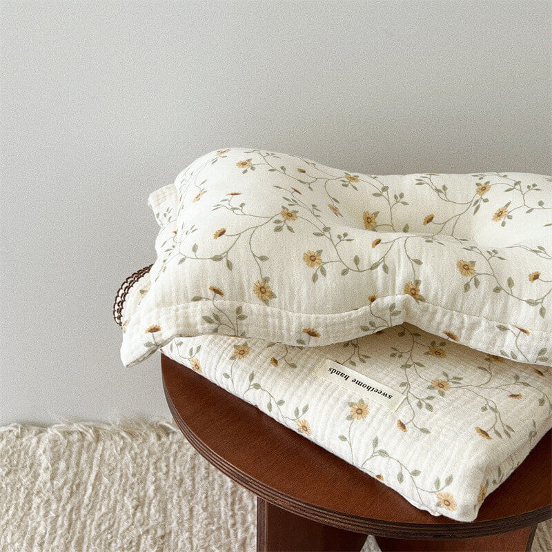 Soft muslin baby pillow and blanket set with a yellow floral pattern, folded on a wooden table.