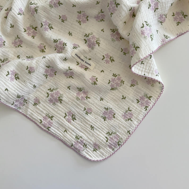 A close-up, top-down view of a soft, purple floral reversible cotton gauze blanket with a small "sweethome hands" label, suitable for baby bedding.