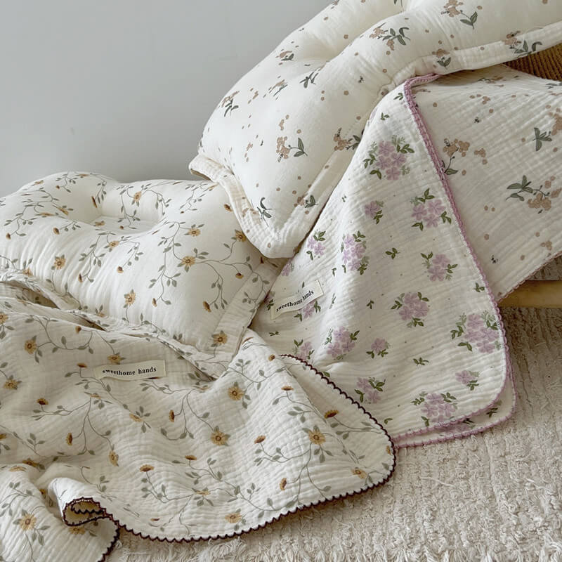 Two reversible cotton gauze baby blankets with pillows, one with a purple floral design and the other a complementary brown floral pattern, for a coordinated nursery.