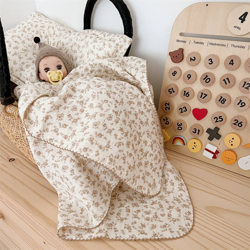 camellia floral muslin baby blanket and pillow set covering a doll in a bassinet.