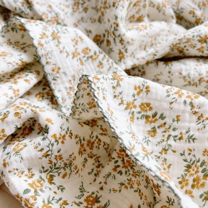 Close-up of a soft, breathable hibiscus floral muslin blanket with a dark green scalloped edge, ideal as a blanket for newborns.
