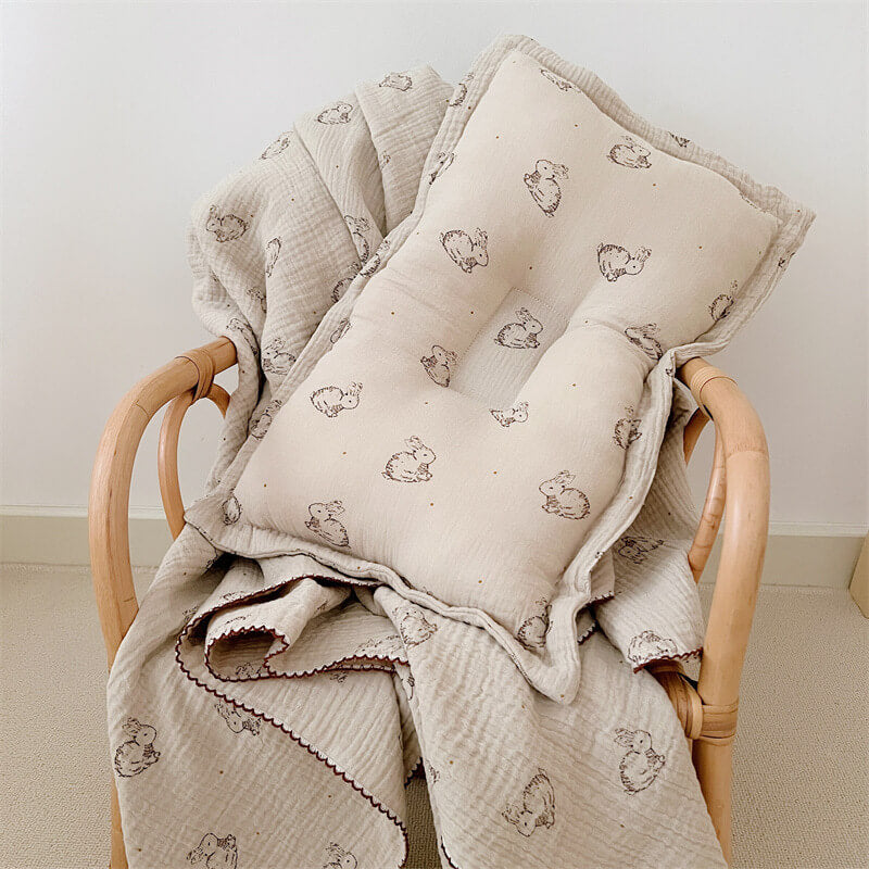 The Bunny cotton muslin baby blanket and pillow set arranged on a wooden nursery chair.