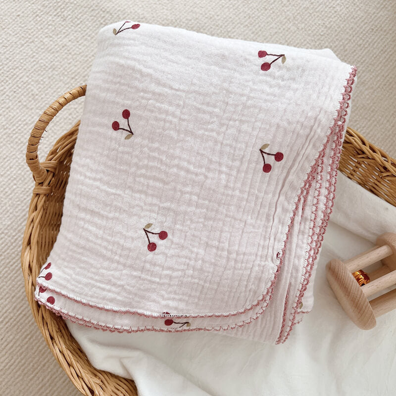 Folded Soft Cherry Blossom cotton muslin baby blanket in a woven basket, featuring the embroidered pattern.
