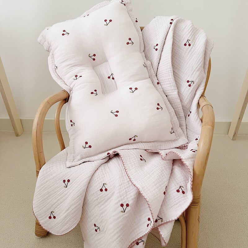 Soft cherry blossom baby blanket and pillow set on a wooden nursery chair.