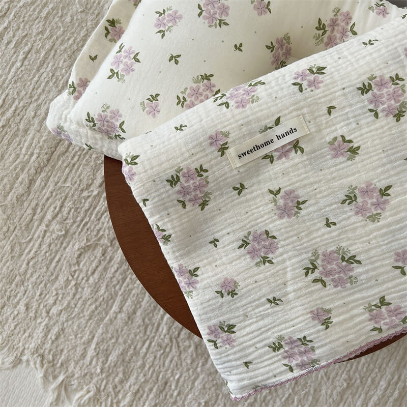 Close-up of a folded purple floral cotton gauze baby blanket, showing the soft, textured fabric and matching pillow.