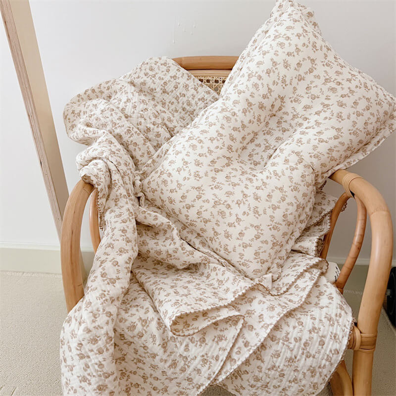 The camellia floral muslin baby blanket and pillow set draped over a wooden chair.