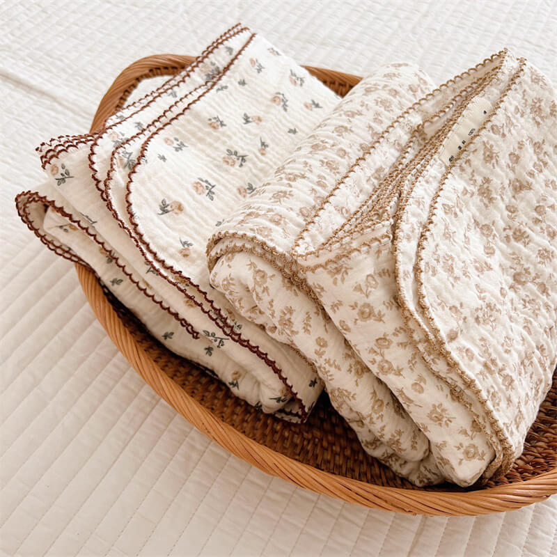folded camellia floral muslin baby blankets with different trim designs in a woven basket.