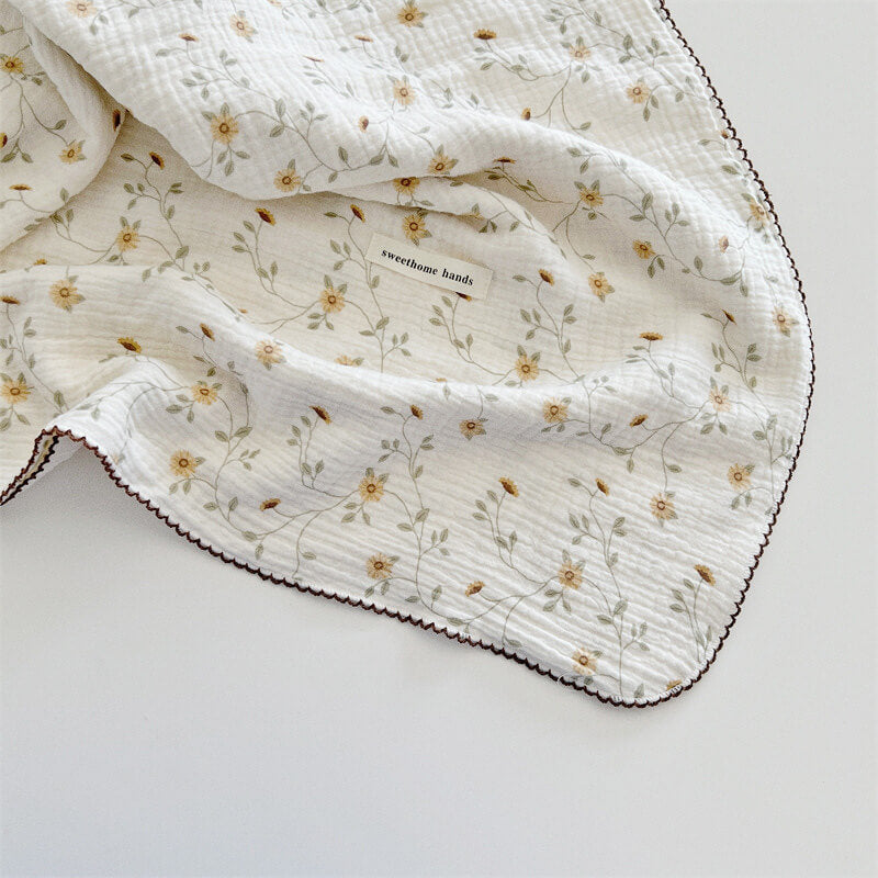 Close-up of the yellow floral muslin baby blanket showing the vine pattern and the scalloped trim.