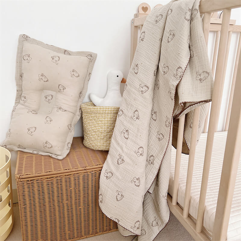 Bunny pattern cotton muslin baby blanket and pillow set displayed in a nursery with a crib.