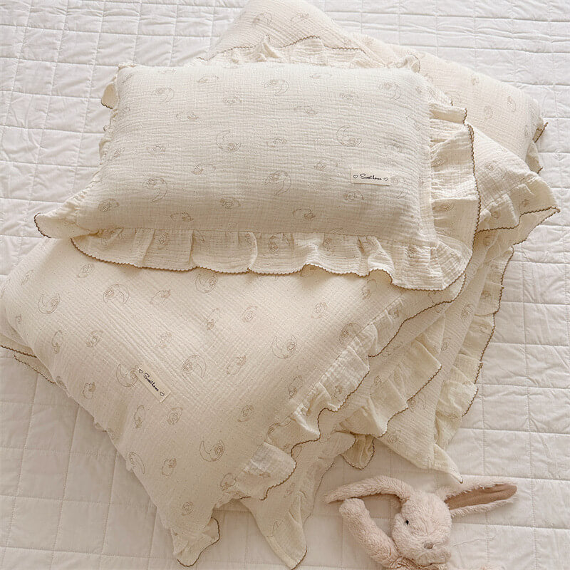 Stack of lamb print ruffle duvet cover and pillowcase in neutral cotton muslin, styled on a white quilted bed
