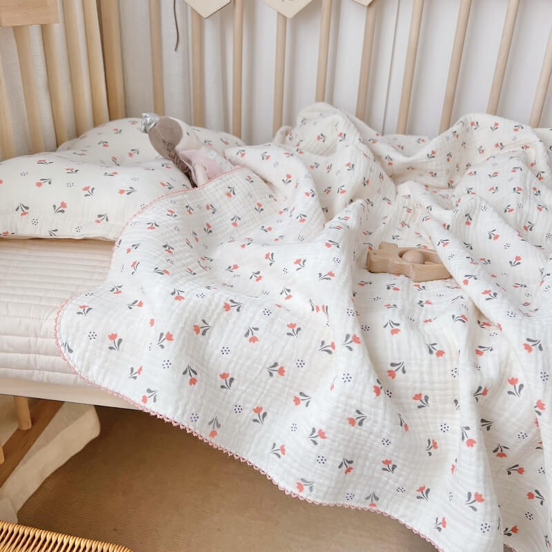 A beautiful tulip floral baby blanket and matching pillow, draped over a crib to show a warm and comforting nursery setting.