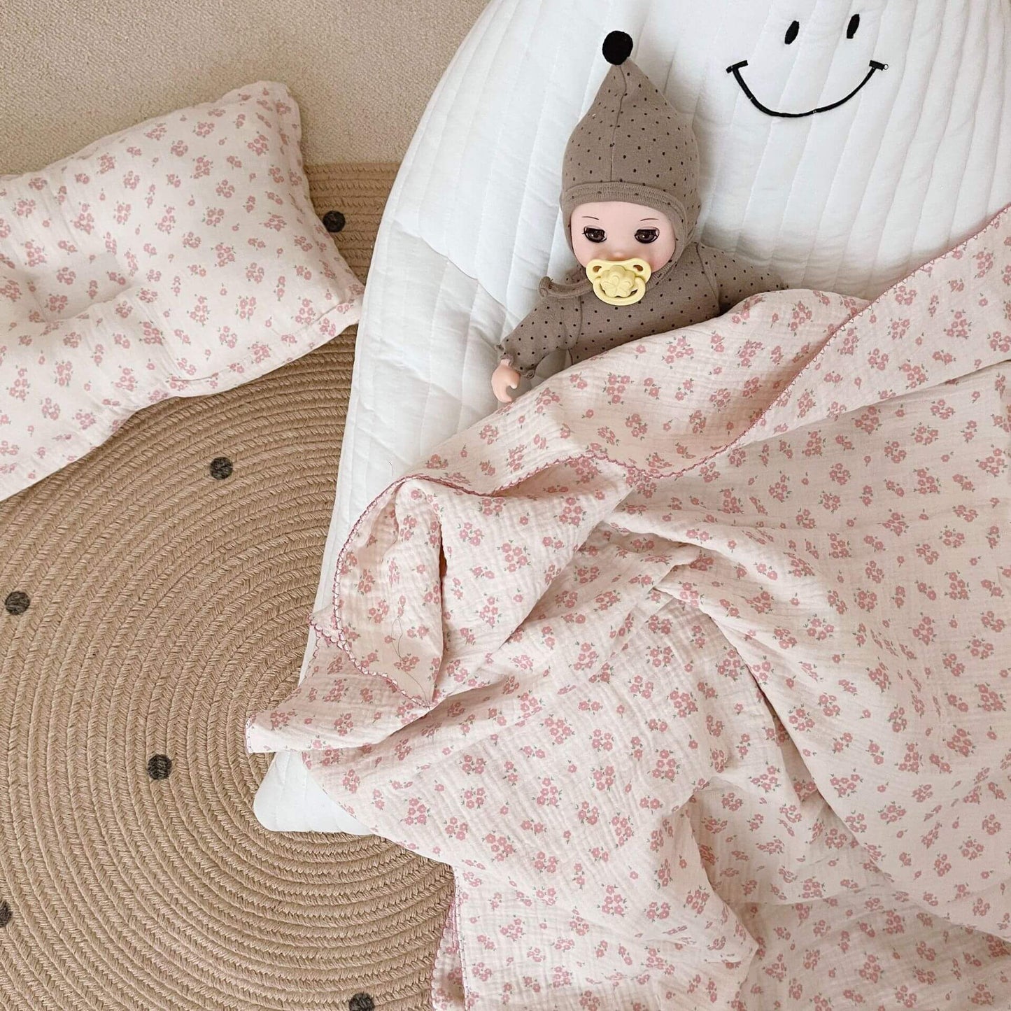 Vintage floral muslin baby blanket and pillow set with a doll on a cloud-shaped cushion.