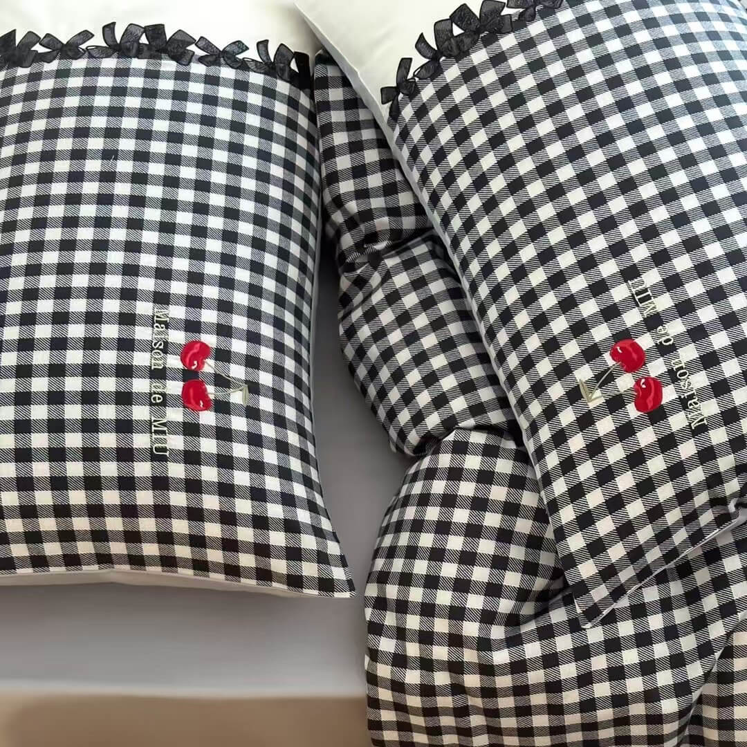 Black and white checkered pillows with red flower embroidery on a neutral background