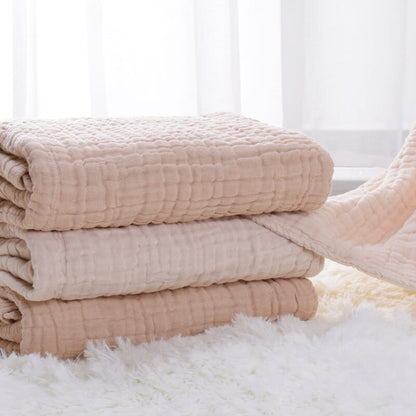 A stack of three neatly folded 6-layer organic colored cotton muslin baby blankets in natural beige, oatmeal, and ivory colors, highlighting the thickness.
