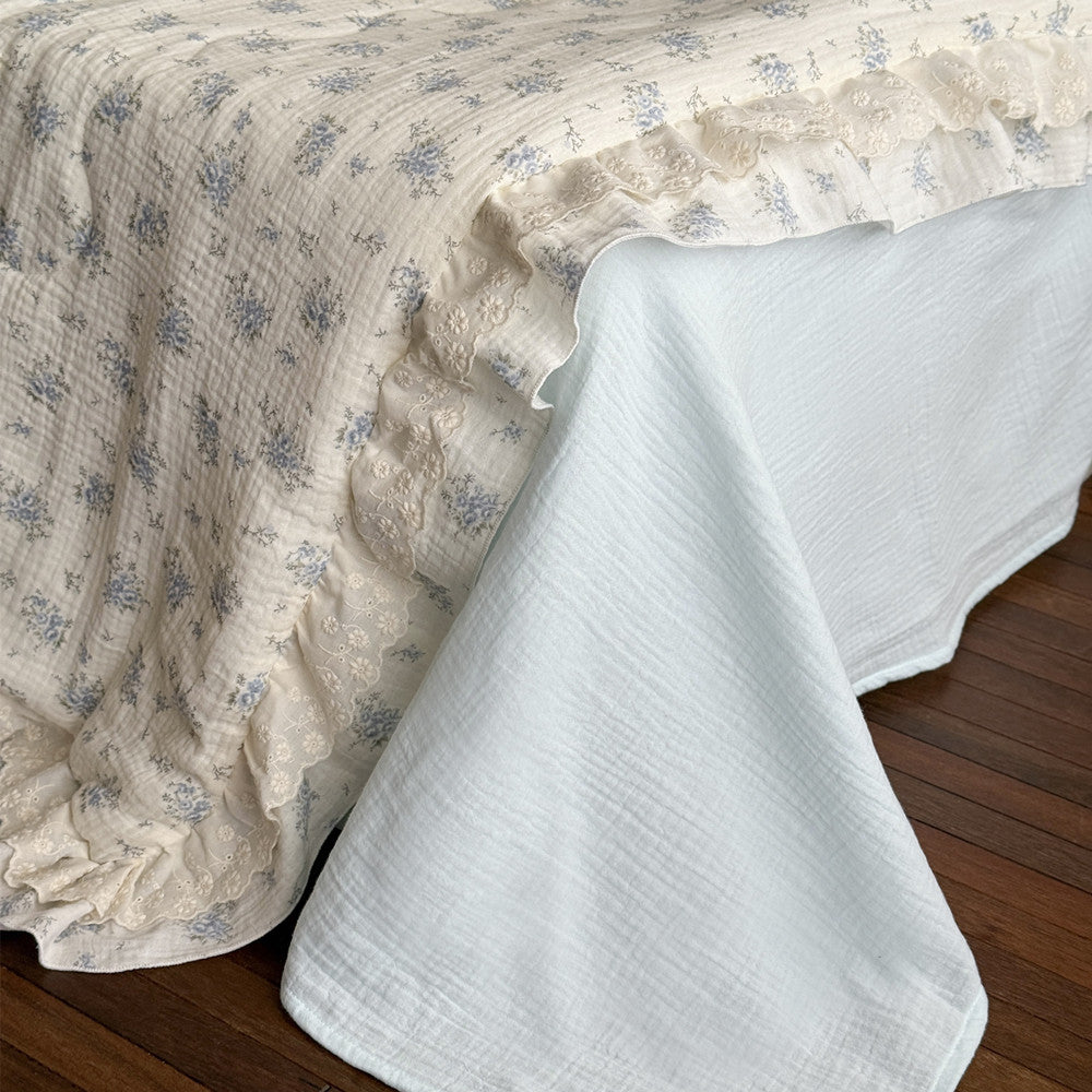 Close-up of ruffled edge and white gauze bed sheet in blue floral cotton comforter
