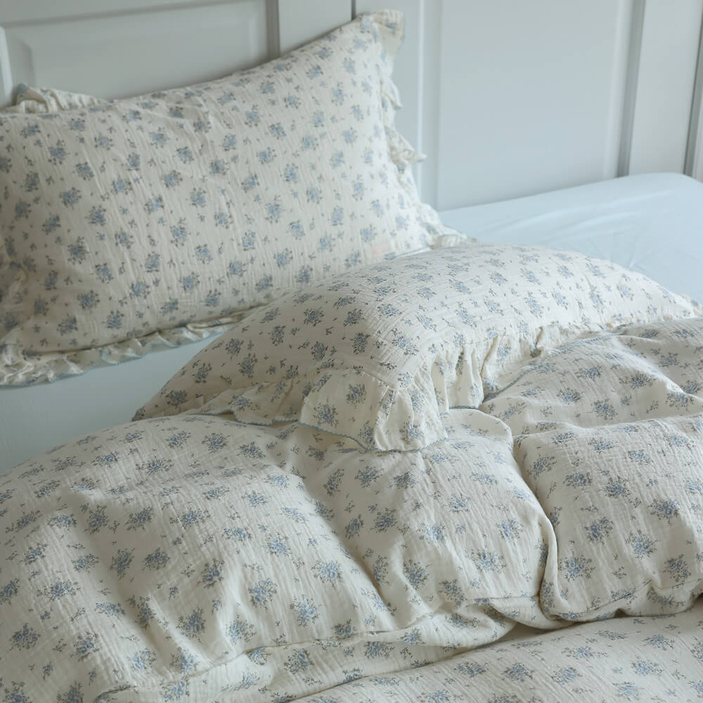 Close-up of blue posy cotton muslin bedding with ruffled pillowcase and soft floral texture