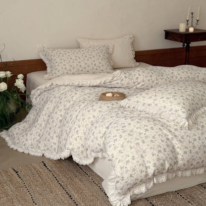 Side angle of a cozy bed dressed with a romantic shabby chic blue floral muslin bedding set, showcasing the comforter's delicate ruffled edges and matching floral pillowcases against a warm wainscot wall.
