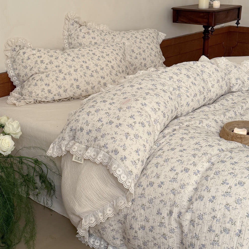 Close-up showing the soft, breathable unbleached muslin backing of a shabby chic comforter, folded over to reveal the elegant blue rose pattern and scalloped lace trim.