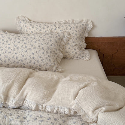 Overhead perspective showing a luxurious layered bed with multiple cream muslin cotton pillows featuring intricate lace ruffles and a complementary blue floral printed comforter.