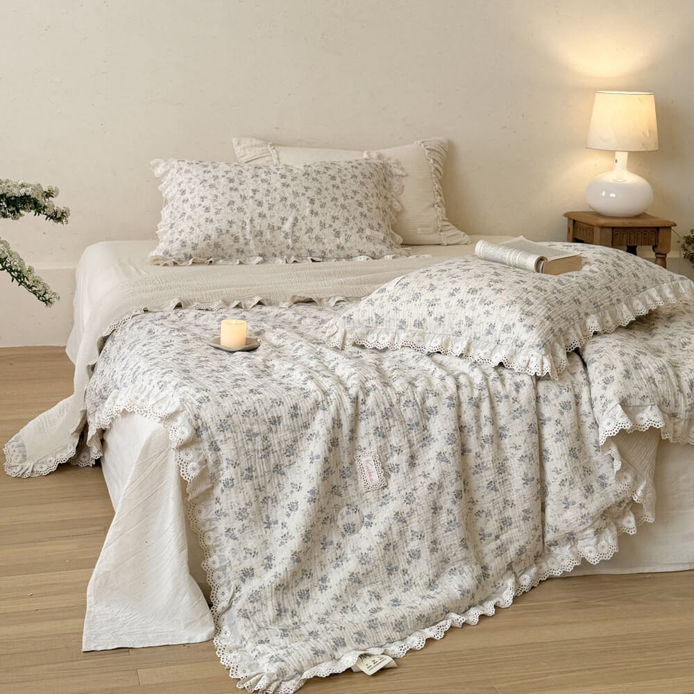 Cozy bedroom styling featuring a blue rose pattern muslin cotton quilt with delicate eyelet lace edges, illuminated by a warm bedside table lamp for a romantic, vintage aesthetic.
