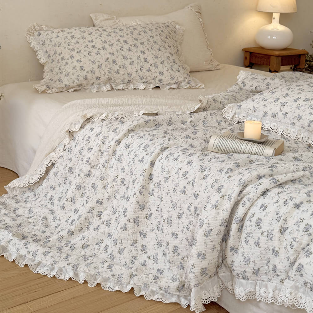 Shabby chic blue floral printed muslin blanket folded over to reveal a soft cream-colored reverse side and exquisite ruffled eyelet lace border detailing.