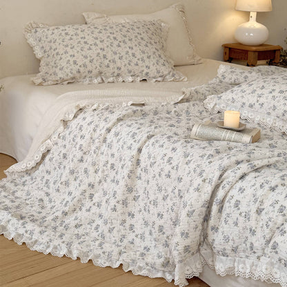 Shabby chic blue floral printed muslin blanket folded over to reveal a soft cream-colored reverse side and exquisite ruffled eyelet lace border detailing.