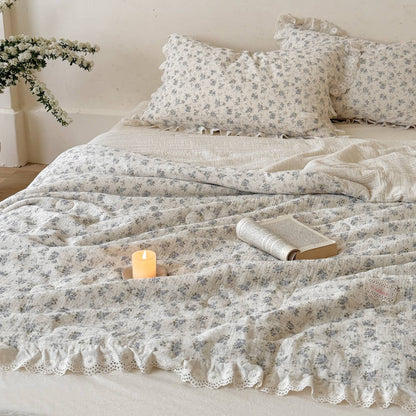 Cozy morning bed setting with a rustic open book and candle resting on a soft, crinkled cotton muslin comforter featuring a delicate blue rose floral pattern.