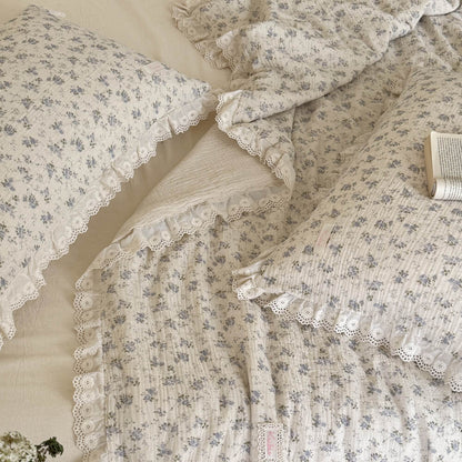 Overhead detail shot of a romantic cottagecore bedding collection, displaying the contrast between the blue floral print and cream muslin reverse with layered eyelet ruffles.