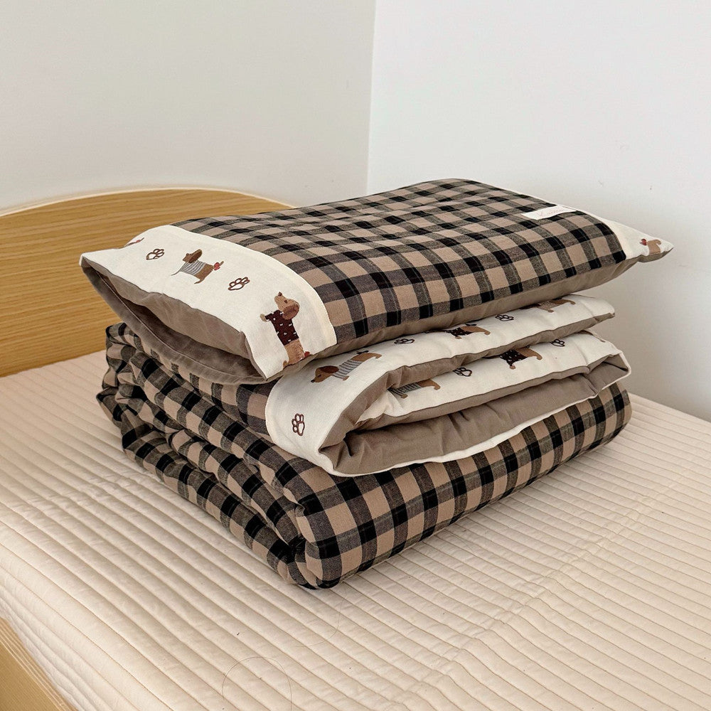 Stack of checkered bedding with embroidered designs on a bed.