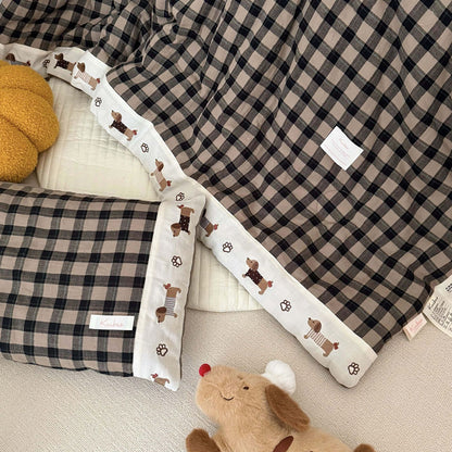 Plaid blanket with embroidered border and plush toy on a checkered surface