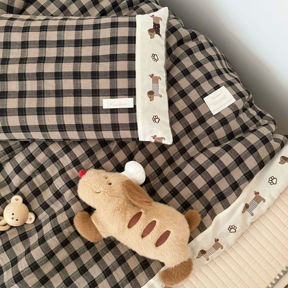 Plaid blanket with a plush toy and decorative pillow on a bed.