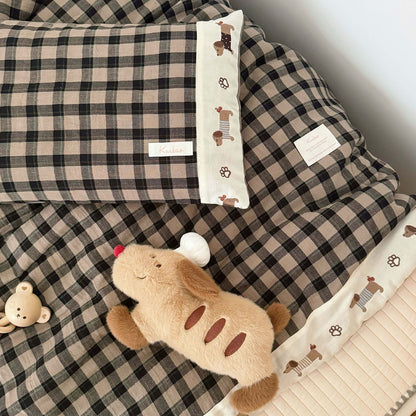 Plaid blanket with a plush toy and decorative pillow on a bed.