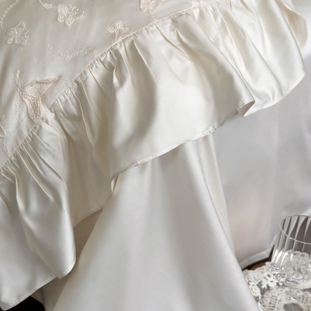 Macro shot of the silky ruffled edge and butterfly embroidery detail on the cream duvet.