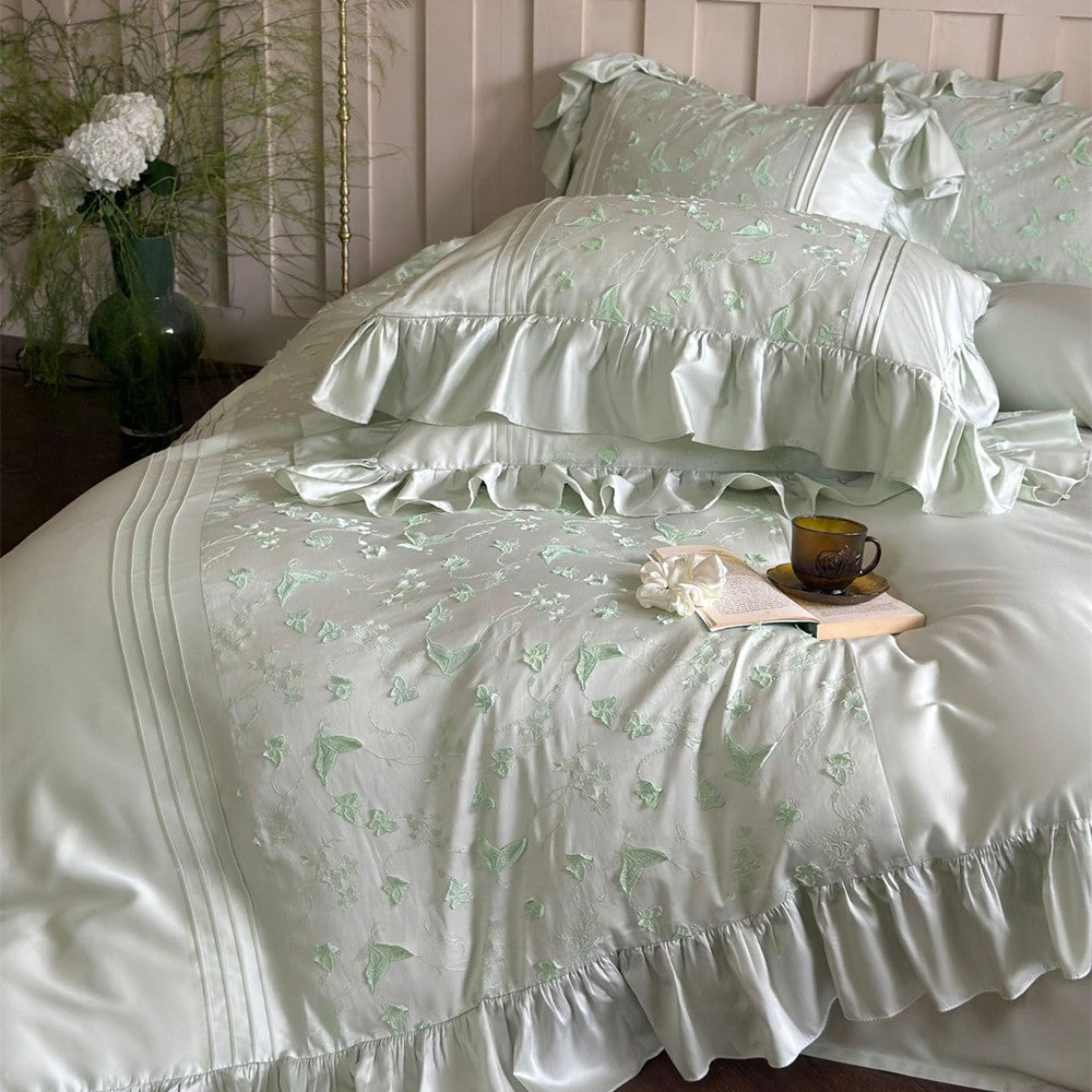 Close-up of light green bedding, featuring ruffles, pintucks, and vibrant butterfly embroidery.