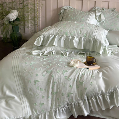 Close-up of light green bedding, featuring ruffles, pintucks, and vibrant butterfly embroidery.