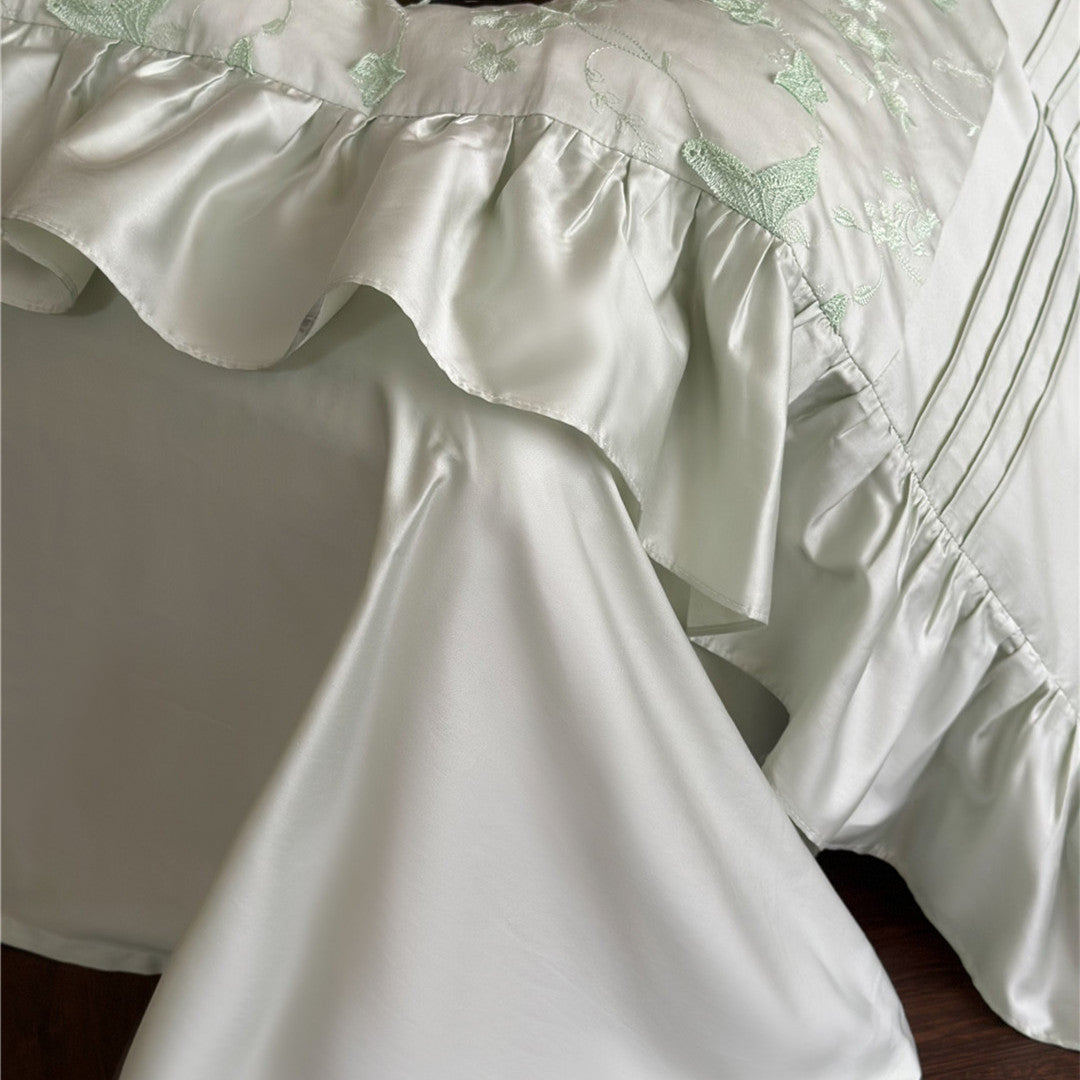 Detail shot of the silky ruffled edge and pleated design on the light green duvet cover.